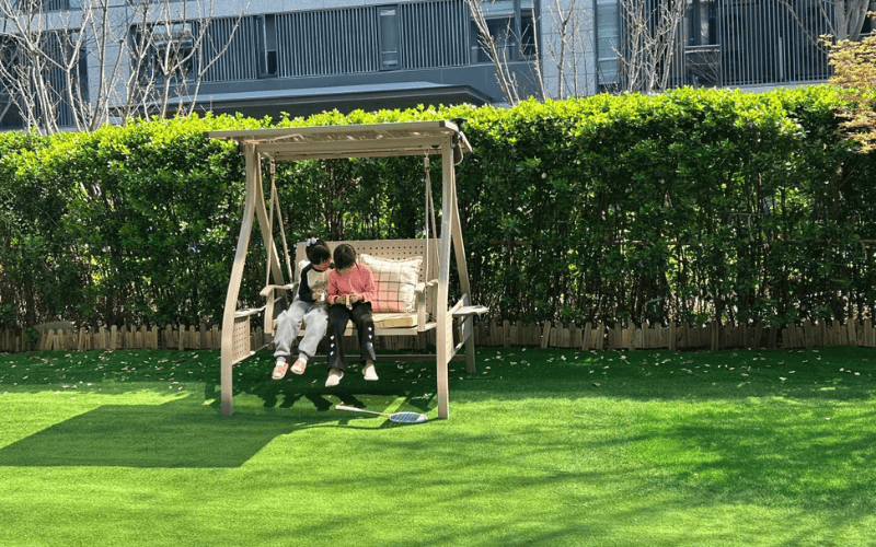 Guía completa para la limpieza del césped artificial 4 Niños sentados en un columpio en un patio residencial con césped artificial