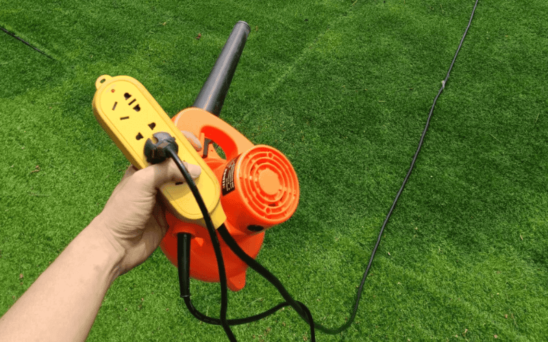 Guía completa para la limpieza del césped artificial 1 Persona sosteniendo un soplador eléctrico y un cable de extensión sobre una superficie de césped artificial