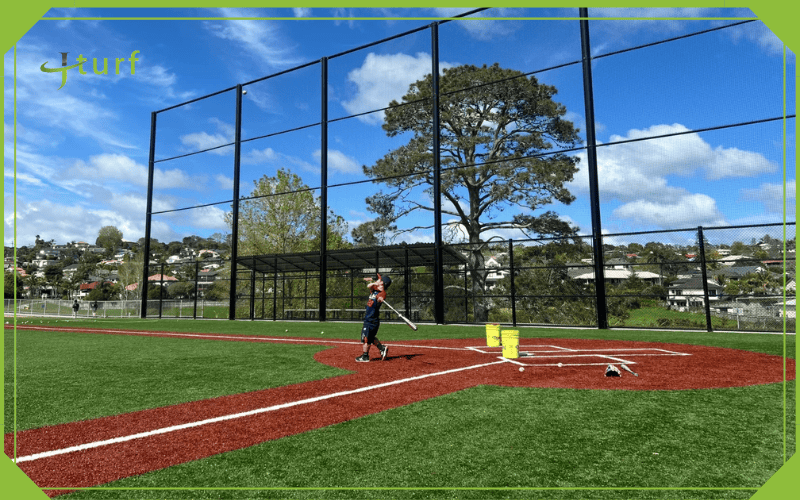 Una mirada clara al costo de construir un campo de béisbol de césped 4 Campo de béisbol de césped sintético con cerca alta y bateador practicando cerca del plato de home