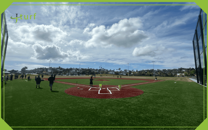 Una mirada clara al costo de construir un campo de béisbol de césped 1 Toma de gran angular de un campo de béisbol de césped con jugadores practicando bajo un cielo nublado
